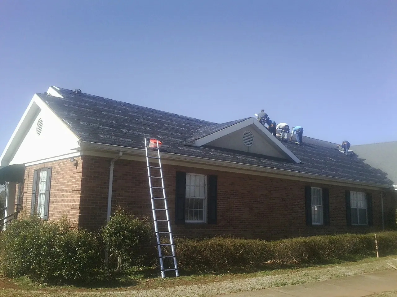 Crew tearing shingles off a brick ranch roof with a ladder set — Metal Roof Repair work by our crew in Williamson